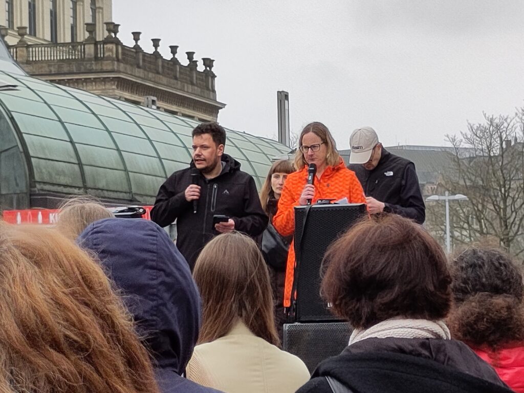 Mehrere Personen auf einer erhöhten Position. Zwei von ihnen halten Mikrofone in ihren Händen.