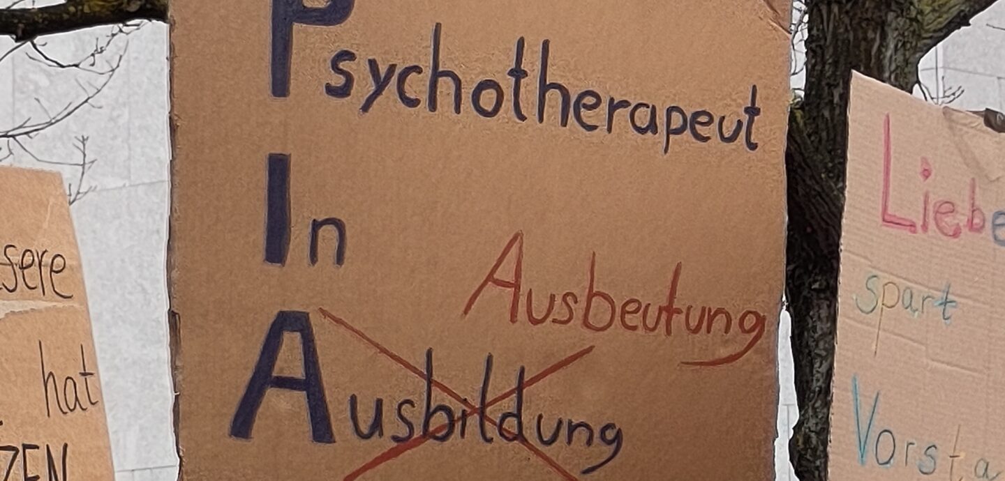 Handschriftliches Plakat mit dem Text „Psychotherapeut In Ausbildung (PIA)“ – das Wort Ausbildung ist ausgekreuzt und durch das Wort „Ausbeutung“ ersetzt.
