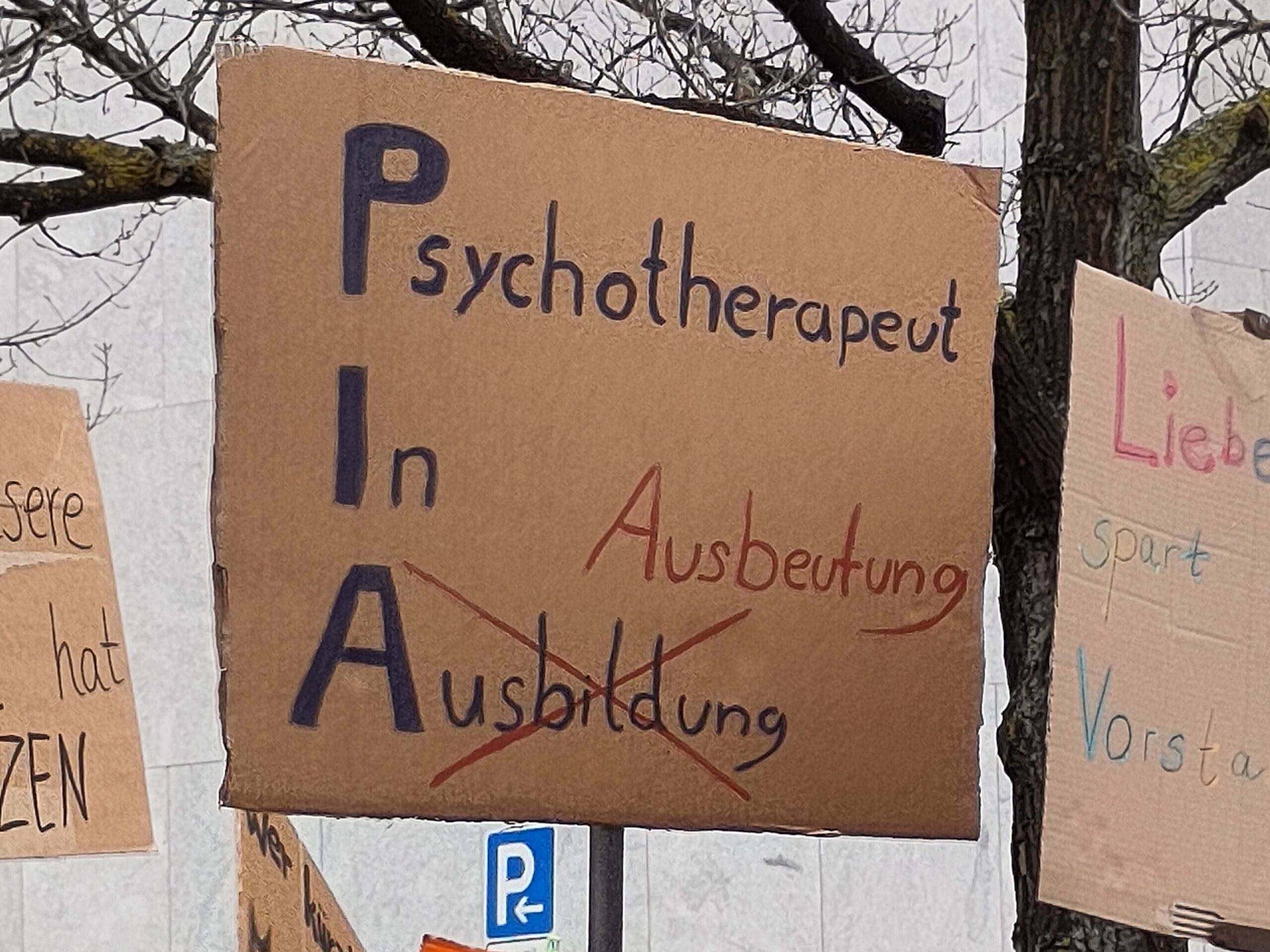 Handschriftliches Plakat mit dem Text „Psychotherapeut In Ausbildung (PIA)“ – das Wort Ausbildung ist ausgekreuzt und durch das Wort „Ausbeutung“ ersetzt.