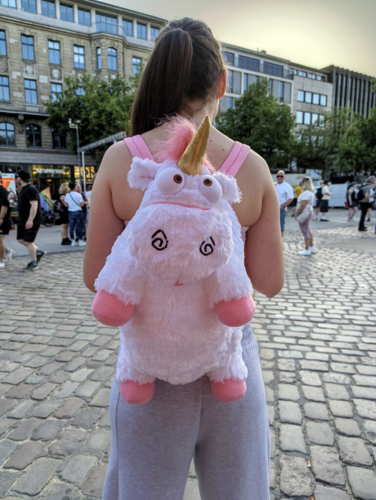 Eine Person trägt auf ihrem Rücken einen Rucksack in Form eines Einhorn-Schafes.